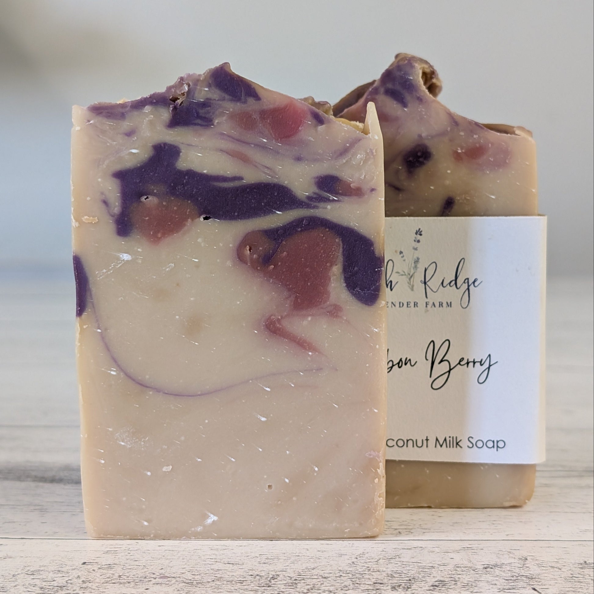 Two soap bars with visible color swatches on a wooden surface, one with a label.