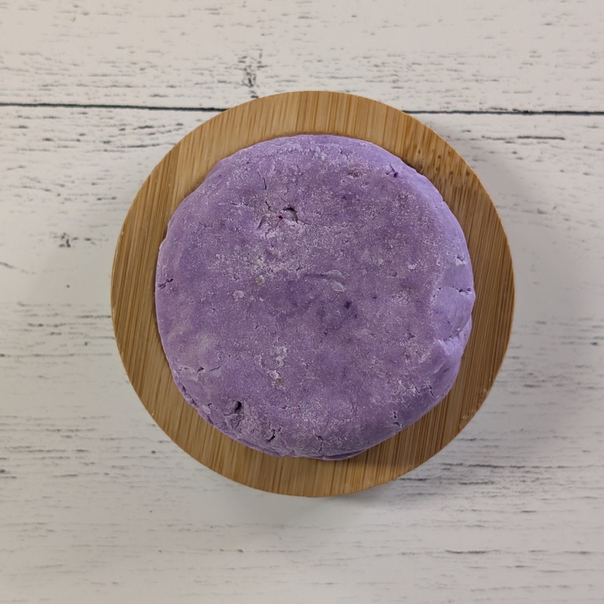 Purple shampoo bar on a wooden coaster with a white wooden surface background