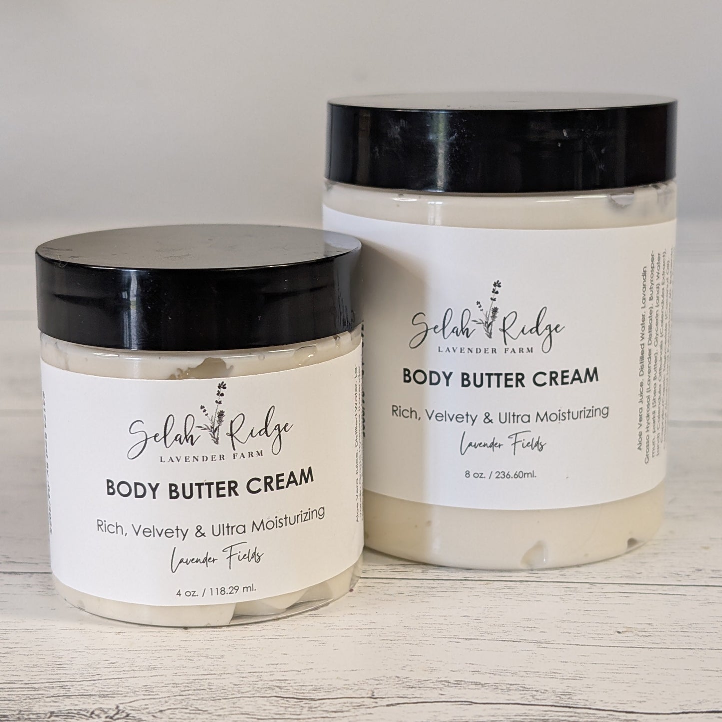 Two jars of body butter cream with black lids on a wooden surface.