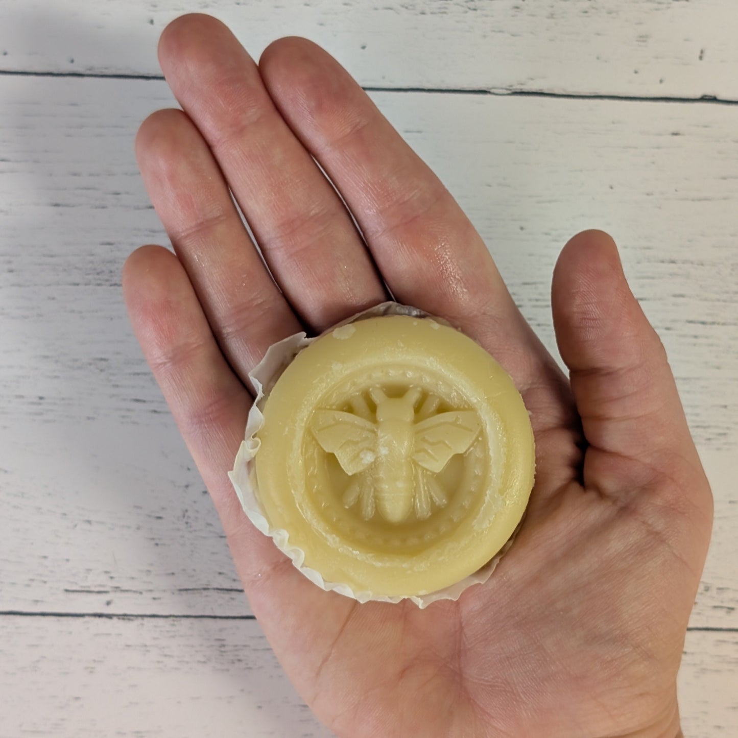 Hand holding a yellow soap bar with a bee design on a light wooden surface