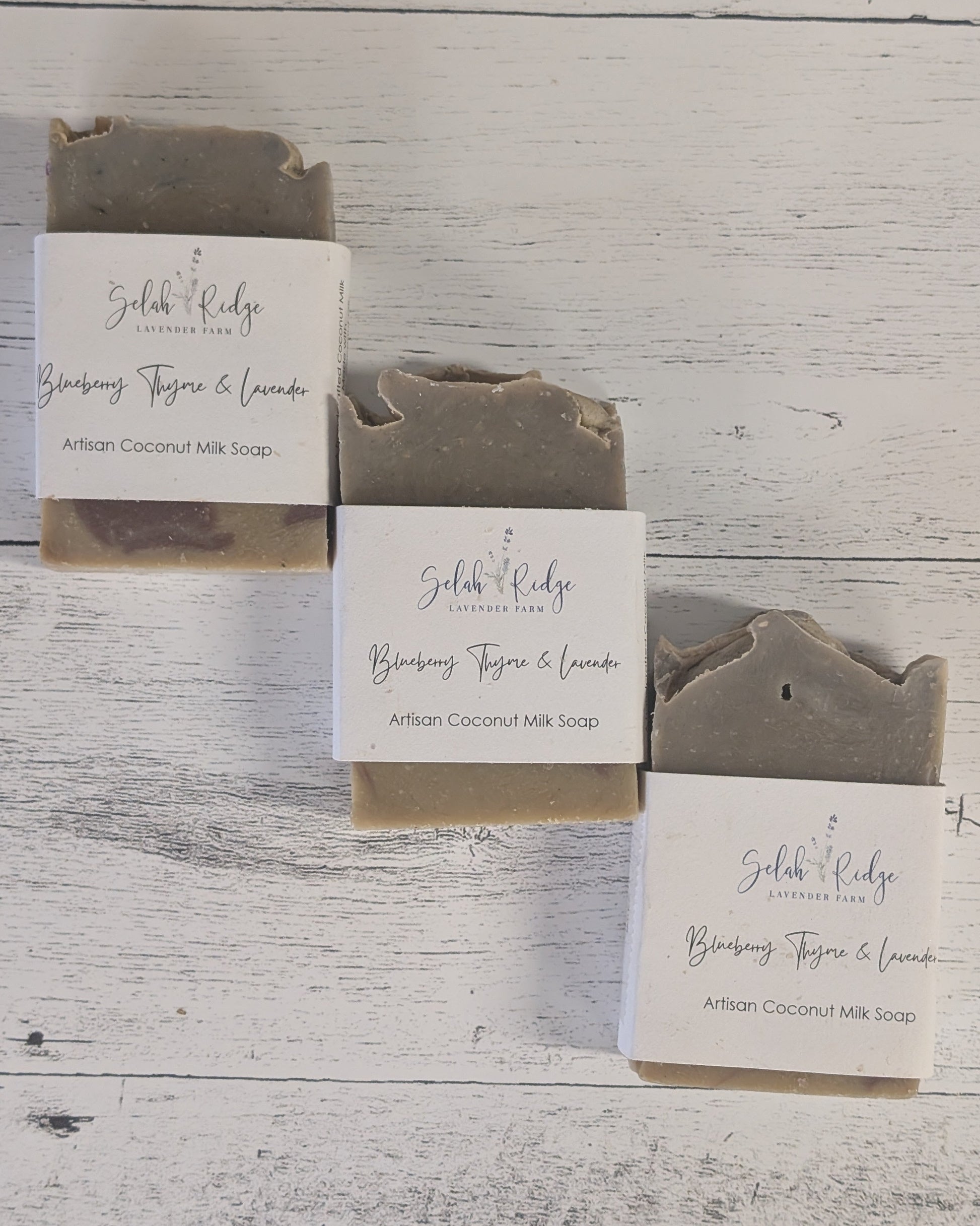 Three bars of soap with packaging on a wooden surface